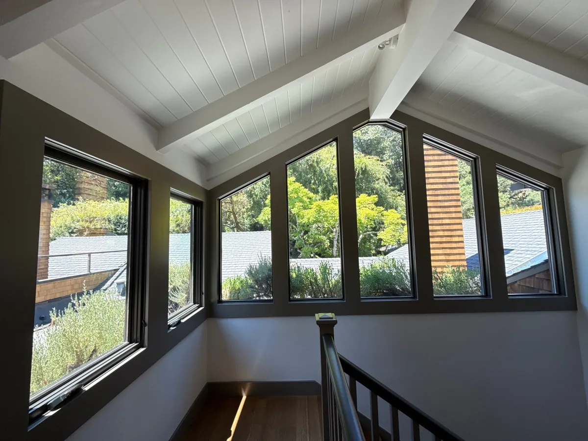 Stair landing with six gable-end windows over rooftops and trees, window film on the glass
